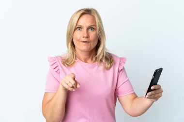 Beyaz arka planda izole edilmiş cep telefonu kullanan orta yaş şaşırmış ve ön tarafı işaret ediyor