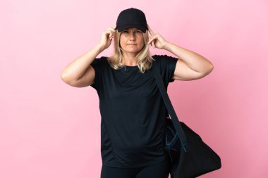 Spor çantalı orta yaşlı bir kadın pembe arka planda izole edilmiş. Şüpheleri ve düşünceleri var.