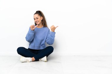 Yerde oturan genç bir kadın bir ürün sunmak için yan tarafı işaret ediyor.