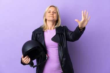 Mor arka planda izole edilmiş motosiklet kaskı tutan orta yaşlı kadın parmaklarıyla beşi sayıyor.