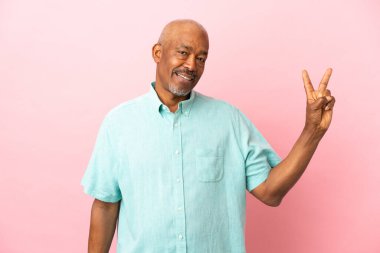 Kübalı son sınıf öğrencisi pembe arka planda izole edilmiş gülümsüyor ve zafer işareti gösteriyor