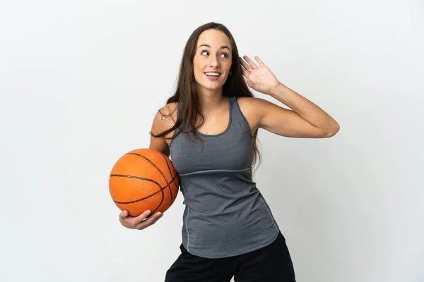 若いです女性プレイバスケットボール上の隔離された白い背景何かに耳を傾けるによって手を置く — ストック写真