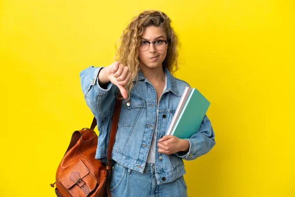 若い学生Caucasian女性は否定的な式で親指を下に示す黄色の背景に隔離されました — ストック写真