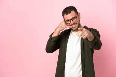 Pembe arka planda izole edilmiş genç Brezilyalı adam telefon hareketleri yapıyor ve ön tarafı işaret ediyor.