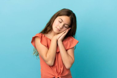 Küçük beyaz kız, mavi arka planda izole edilmiş bir şekilde uyku jesti yapıyor.