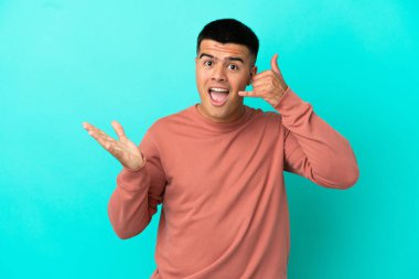 Soyutlanmış mavi arka planda genç yakışıklı bir adam telefon jesti yapıyor ve şüpheci