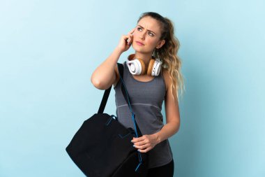Spor çantalı genç Brezilyalı kadın mavi arka planda izole edilmiş. Şüpheleri var.
