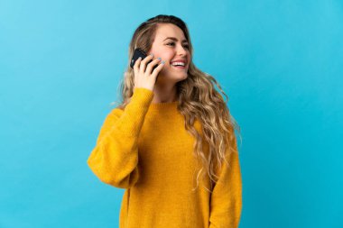 Mavi arka planda izole edilmiş genç Brezilyalı kadın cep telefonuyla sohbet ediyor.