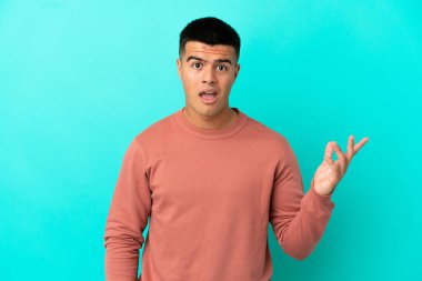 Soyutlanmış mavi arka planda genç yakışıklı adam şüpheli hareketler yapıyor.