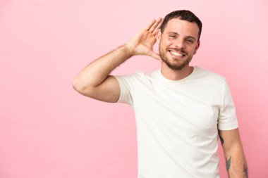 Pembe arka planda izole edilmiş genç Brezilyalı bir adam. Kulağına elini sürerek bir şeyler dinliyor.