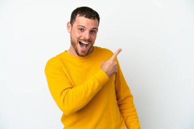 Beyaz arka planda izole edilmiş genç Brezilyalı adam şaşırmış ve işaret ediyor.