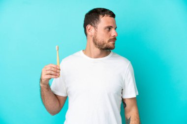 Mavi arka planda izole edilmiş dişlerini fırçalayan Brezilyalı genç adam yan tarafa bakıyor.