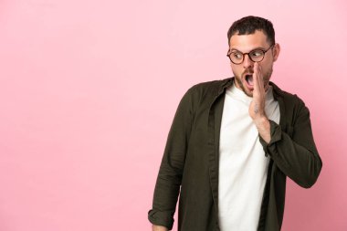 Pembe arka planda izole edilmiş genç Brezilyalı adam yan tarafa bakarken sürpriz bir jest yapıyor.