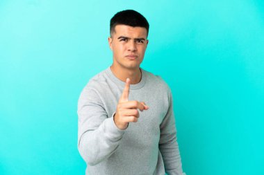 Soyutlanmış mavi arka plan üzerinde genç yakışıklı adam hayal kırıklığına uğramış ve ön tarafı işaret ediyor.