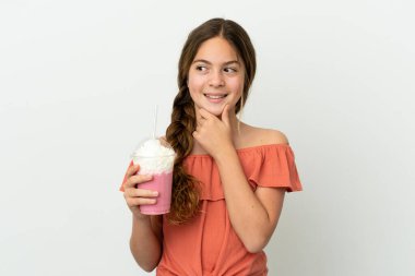 Beyaz arka planda izole edilmiş çilekli milkshake 'li küçük beyaz kız yan bakıyor ve gülümsüyor.