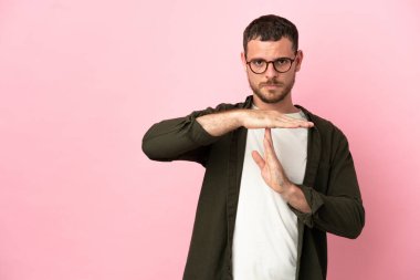 Pembe arka planda izole edilmiş Brezilyalı genç bir adam zaman aşımı hareketi yapıyor.