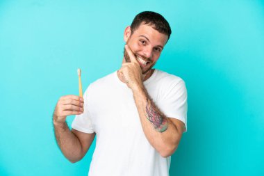 Mavi arka planda izole edilmiş diş fırçalayan genç Brezilyalı adam mutlu ve gülümsüyor.