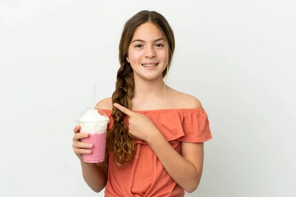小さなCaucasian女の子とともにイチゴミルクシェイク孤立した上に白い背景を指す側に製品を提示 — ストック写真