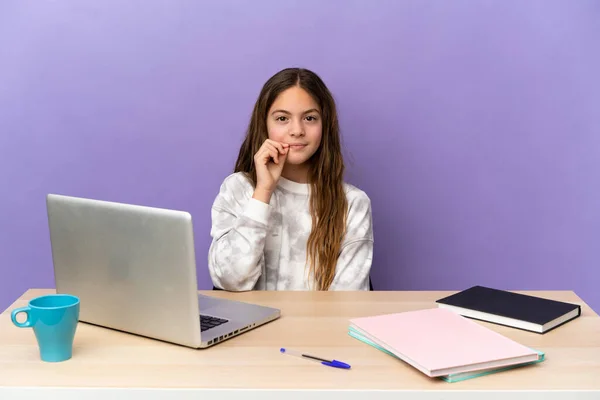 Little student girl in a workplace with a laptop isolated on purple background showing a sign of silence gesture