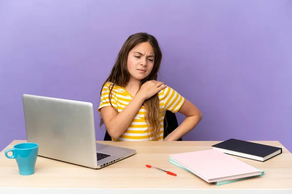 Little student girl in a workplace with a laptop isolated on purple background suffering from pain in shoulder for having made an effort
