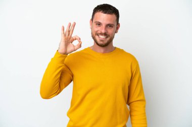 Beyaz arka planda izole edilmiş genç Brezilyalı adam parmaklarıyla tamam işareti gösteriyor