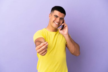 Genç yakışıklı adam, izole edilmiş mor arka planda cep telefonu kullanıyor ve para hareketi yapıyor.