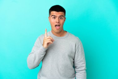 Soyutlanmış mavi arka planı olan genç yakışıklı bir adam parmağını kaldırarak çözümü bulmaya çalışıyor.