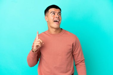 Soyutlanmış mavi arka planda genç yakışıklı adam yukarı bakıyor ve şaşırıyor