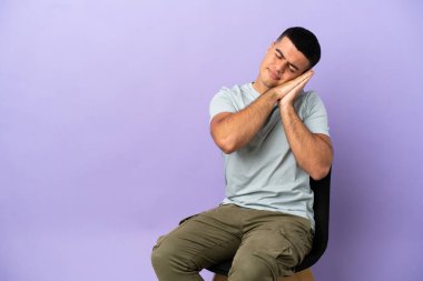 Arka planda izole edilmiş bir sandalyede oturan genç adam hareketli bir uyku hareketi yapıyor.