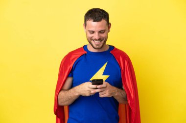 Süper kahraman Brezilyalı adam sarı arkaplanda izole edilmiş cep telefonuyla mesaj gönderiyor.