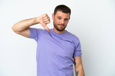 Beyaz arka planda izole edilmiş genç Brezilyalı adam olumsuz ifadeyle baş parmağını aşağı gösteriyor.