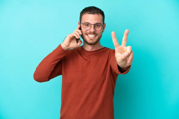 Młody Brazylijczyk Pomocą Telefonu Komórkowego Odizolowany Niebieskim Tle Uśmiechając Się — Zdjęcie stockowe