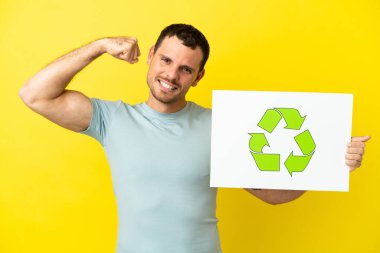 İzole edilmiş mor arka plan üzerinde Brezilyalı bir adam elinde geri dönüşüm simgesi olan bir levha tutuyor ve güçlü bir hareket yapıyor.