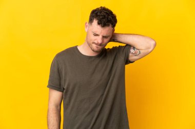 Sarı arka planda boynu ağrıyan, beyaz, yakışıklı genç bir adam.