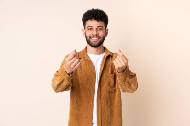 Bej arka planda izole genç Faslı adam para hareketi yapıyor.