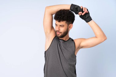 Faslı genç bir adam mavi arka planda izole edilmiş, kolunu uzatıyor.