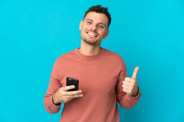 Beyaz tenli yakışıklı adam mavi arka planda izole edilmiş. Cep telefonu kullanıyor.