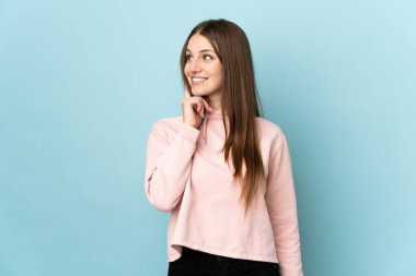 Kafkasyalı genç bir kadın mavi arka planda izole edilmiş bir şekilde yukarı bakarken bir fikir düşünüyor.