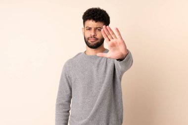 Bej arka planda izole edilmiş genç Faslı adam dur hareketi yapıyor.