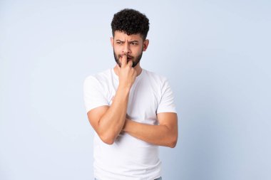 Faslı genç bir adam mavi arka planda izole edilmiş gergin ve korkmuş.