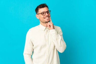Kafkasyalı yakışıklı genç adam mavi arka planda izole edilmiş bir şekilde yukarı bakarken bir fikir düşünüyor.