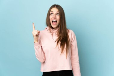 Mavi arka planda izole edilmiş genç beyaz kadın yukarı bakıyor ve şaşırıyor.