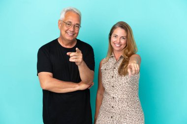 Mavi arka planda izole edilmiş orta yaşlı çift parmaklarını kendine güvenen bir ifadeyle sana gösteriyor.