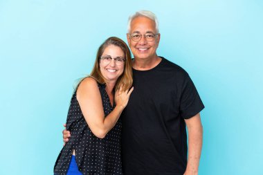 Orta yaşlı çift mavi arka planda gülüyor.