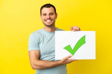 İzole edilmiş mor arkaplan üzerinde Brezilyalı bir adam elinde mutlu ifade ile yeşil onay işareti simgesi olan bir pankart tutuyor