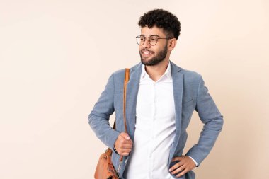 Genç Faslı iş adamı bej arka planda izole edilmiş. Kolları kalçasında ve gülümsüyor.