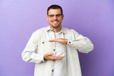 İzole edilmiş mor arkaplan üzerinde Brezilyalı bir adam, bir reklam koymak için avuç içinde hayali bir metin tutuyor.