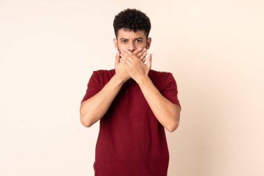 Bej arka planda izole edilmiş genç Faslı adam elleriyle ağzını kapatıyor.