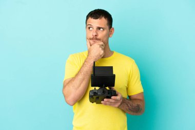 Brezilyalı adam uzaktan kumandayla izole edilmiş mavi arkaplanı kontrol ediyor. Şüpheleri ve düşünceleri var.