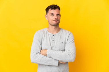 Beyaz tenli yakışıklı adam sarı arka planda izole edilmiş, yukarı bakarken şüpheleri var.